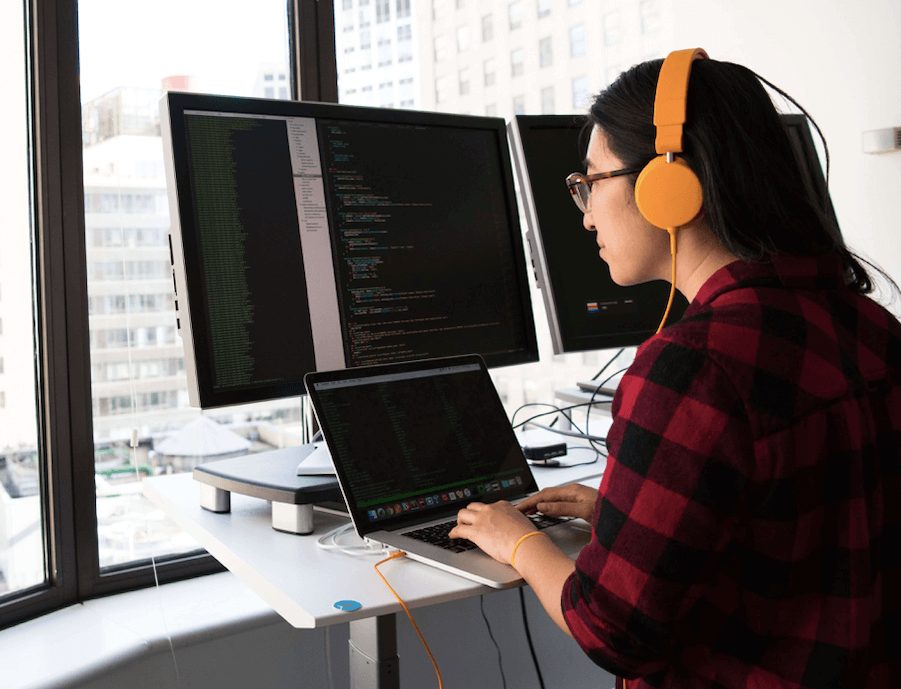 Girl wearing headphones working in front of computer screens.