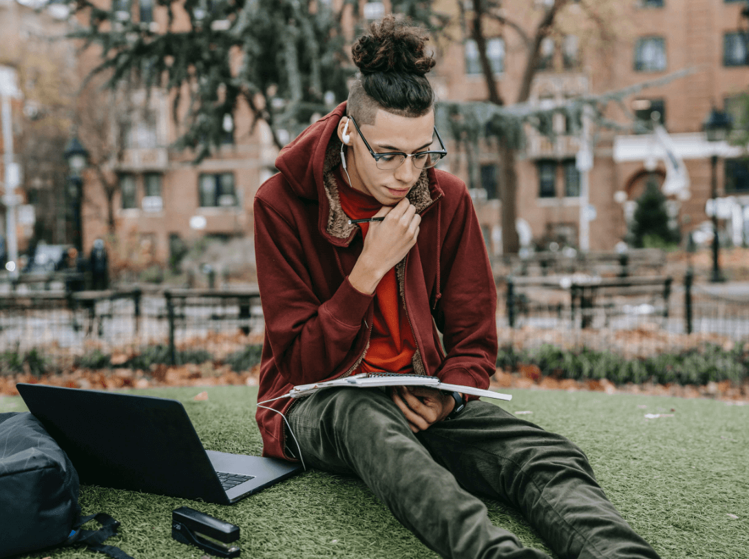College students doing his homework on the grass.