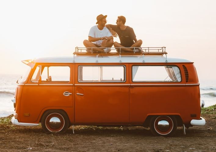 Two guys sitting on top of a travel van. 