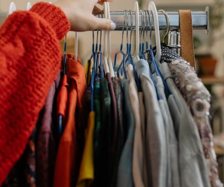 Hand touching clothes on rack.